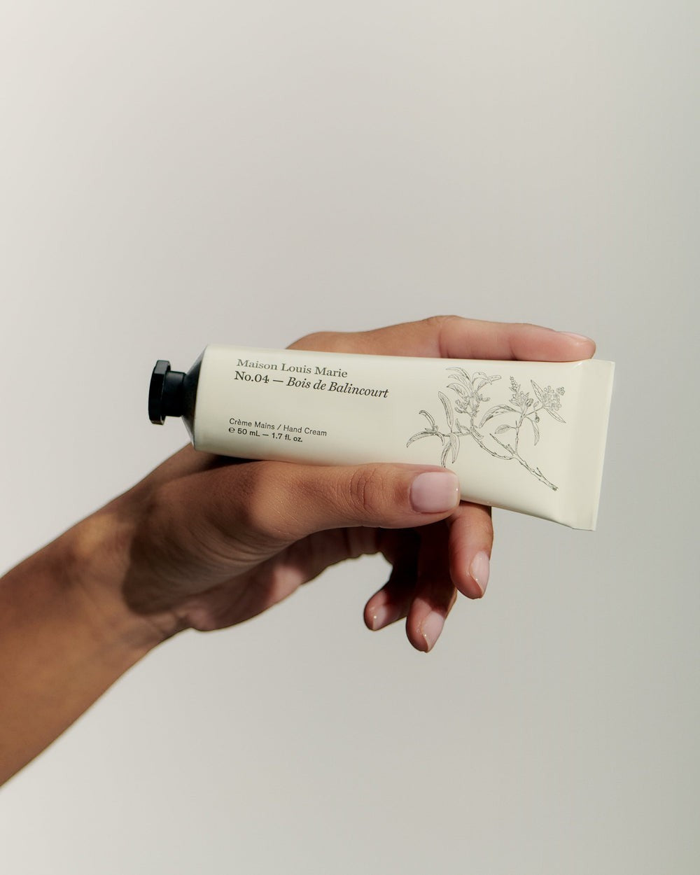 JONES + CO No.04 Bois de Balincourt hand cream tube with botanical illustration, held by a hand.
