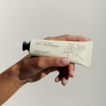 JONES + CO No.04 Bois de Balincourt hand cream tube with botanical illustration, held by a hand.