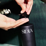 JONES + CO black matte bottle of The Hand Exfoliant with Bergamot, Verbena, Vetiver scent being dispensed into a hand.