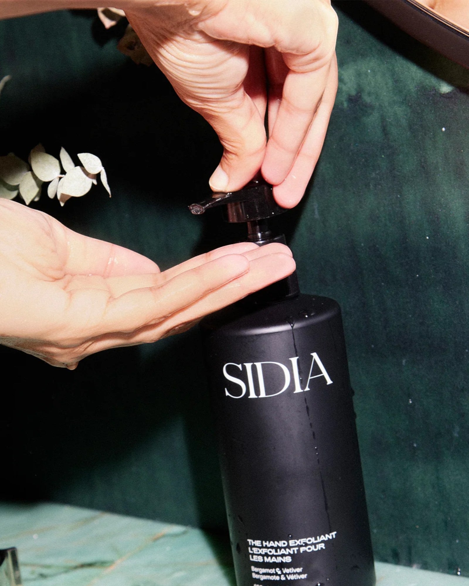 JONES + CO black matte bottle of The Hand Exfoliant with Bergamot, Verbena, Vetiver scent being dispensed into a hand.