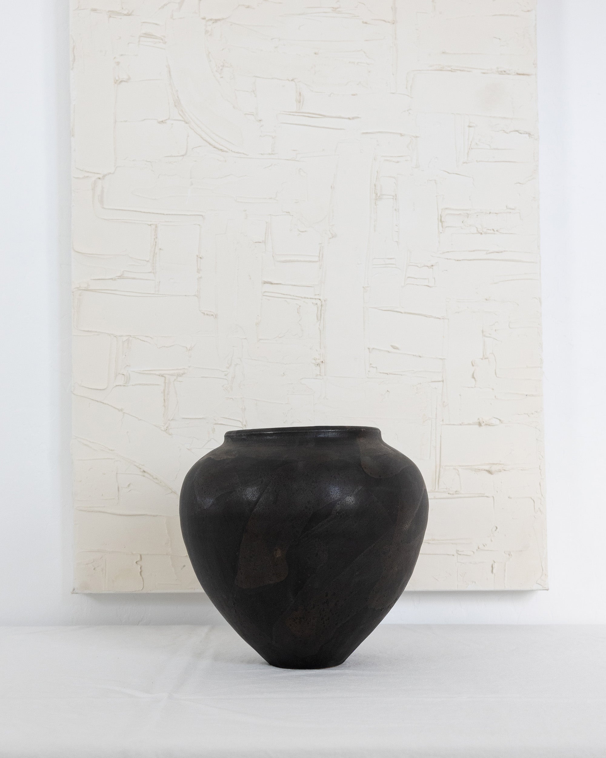 JONES + CO handthrown black ceramic vase with a rounded sculptural shape, displayed against a textured white canvas.