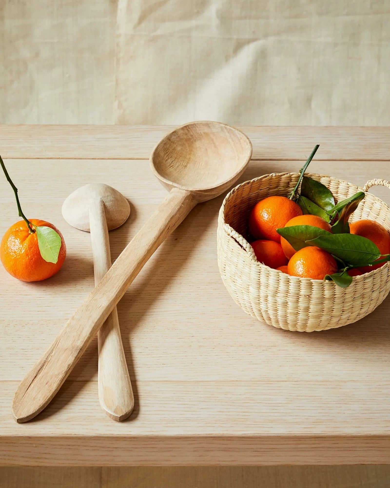 JONES + CO handwoven natural junco petite basket filled with clementines, next to wooden spoons.
