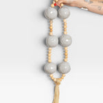 JONES + CO grey ceramic and wood beaded hanging wall art with tassel detail.