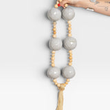 JONES + CO grey ceramic and wood beaded hanging wall art with tassel detail.