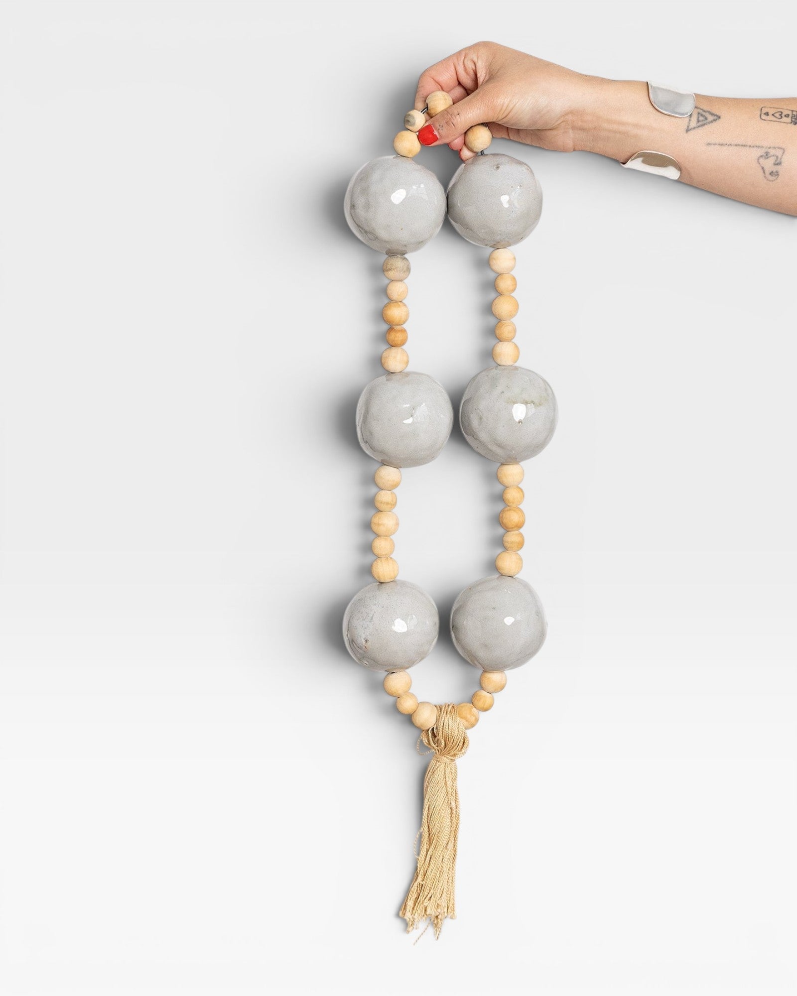 JONES + CO grey ceramic and wood beaded hanging wall art with tassel detail.