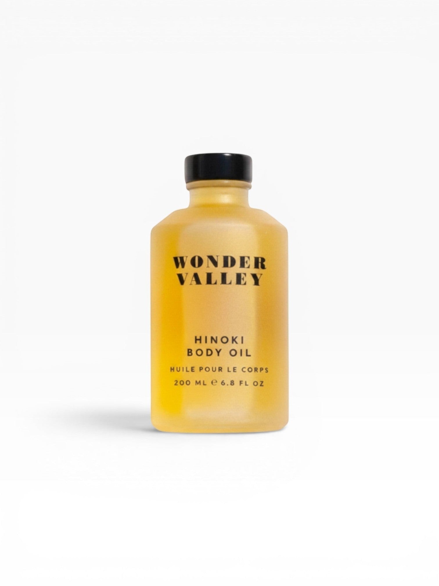 JONES + CO Hinoki Body Oil in a clear glass bottle with a black cap. The oil is golden yellow and has a subtle shimmer.