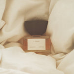 JONES + CO I-Dream Eau de Parfum in a glass bottle with a dark cap, nestled in soft, cream-colored fabric.