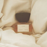 JONES + CO I-Dream Eau de Parfum in a glass bottle with a dark cap, nestled in soft, cream-colored fabric.