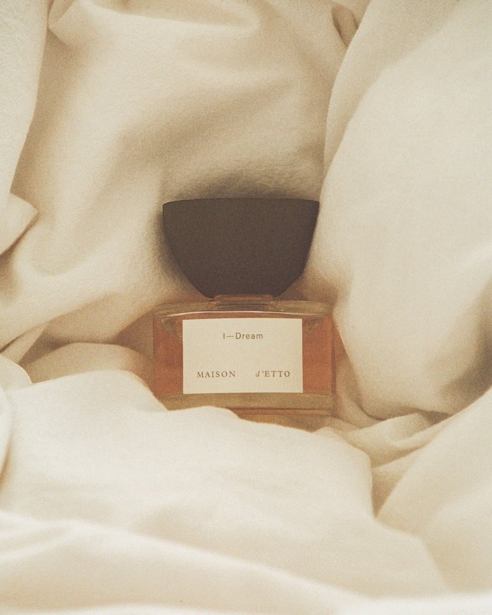 JONES + CO I-Dream Eau de Parfum in a glass bottle with a dark cap, nestled in soft, cream-colored fabric.