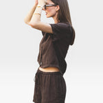 JONES + CO Ida Linen Short in chestnut brown, featuring a drawstring waist and relaxed fit. Model wears sunglasses and jewelry.