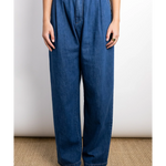 JONES + CO indigo denim Hede pants with high waist, wide leg, front pleats, and side pockets. Model wears them with a gold ring.