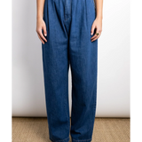 JONES + CO indigo denim Hede pants with high waist, wide leg, front pleats, and side pockets. Model wears them with a gold ring.