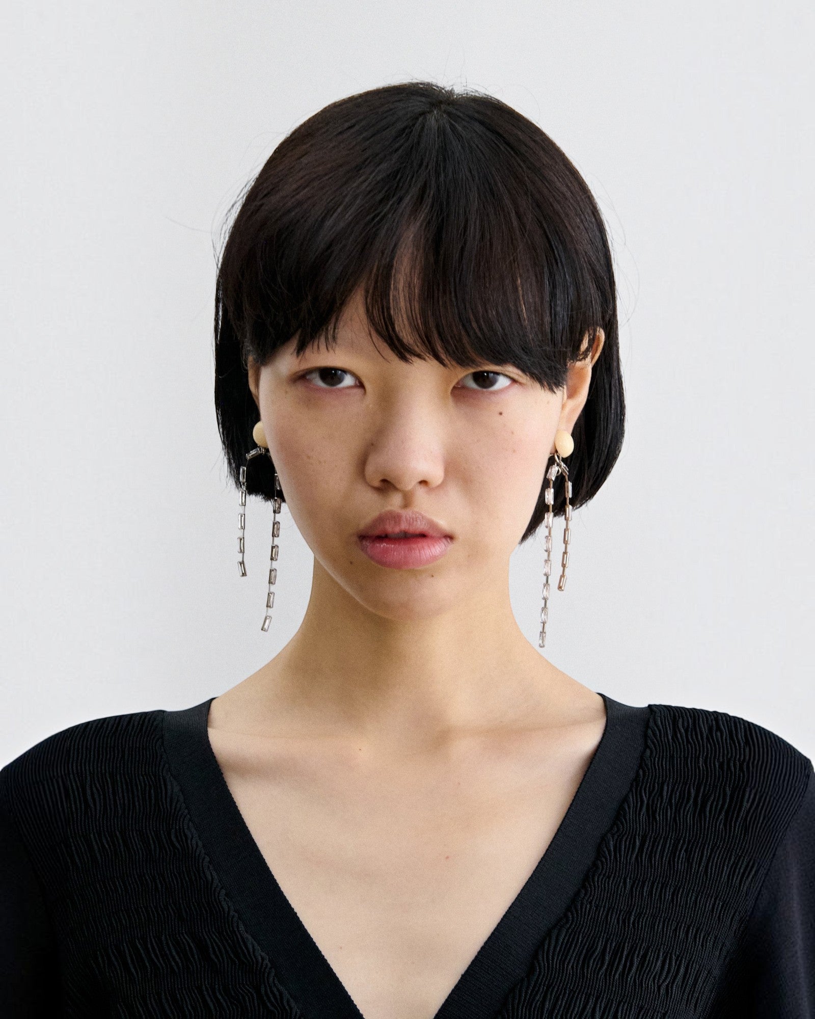JONES + CO Rachel Comey ivory acrylic and brass draped baguette drop earrings worn by a model.