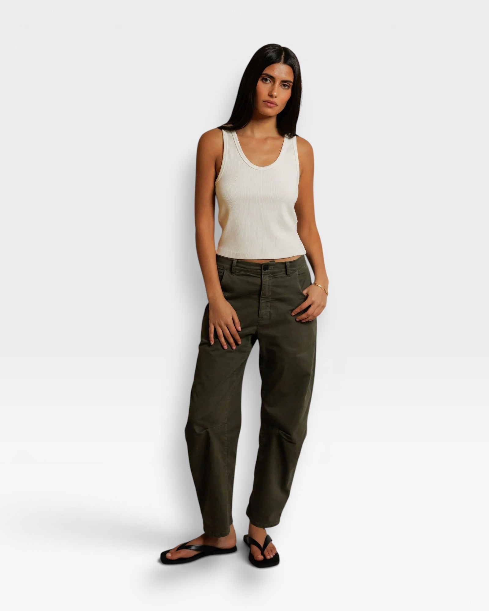 Model wearing a JONES + CO bright ivory ribbed cotton tank top with a scoop neckline paired with olive green pants.
