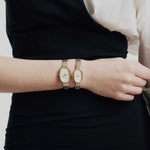 JONES + CO Jane Small Tethered watch in gold with a champagne mother of pearl dial and woven mesh bracelet on a wrist