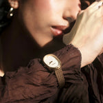 JONES + CO Jane Tethered watch with a gold oval case, champagne mother-of-pearl dial, and woven mesh bracelet on wrist