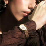 JONES + CO Jane Tethered watch with a gold oval case, champagne mother-of-pearl dial, and woven mesh bracelet on wrist