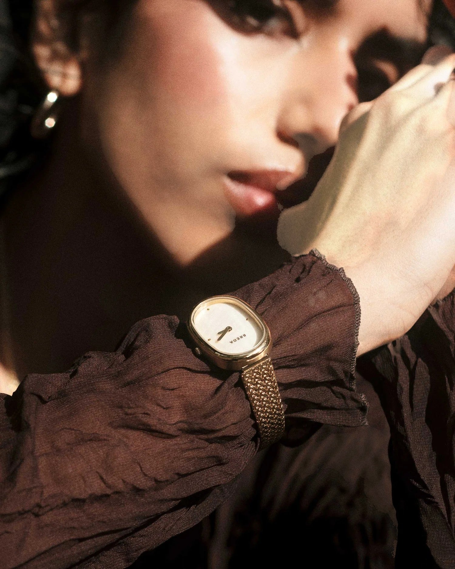 JONES + CO Jane Tethered watch with a gold oval case, champagne mother-of-pearl dial, and woven mesh bracelet on wrist