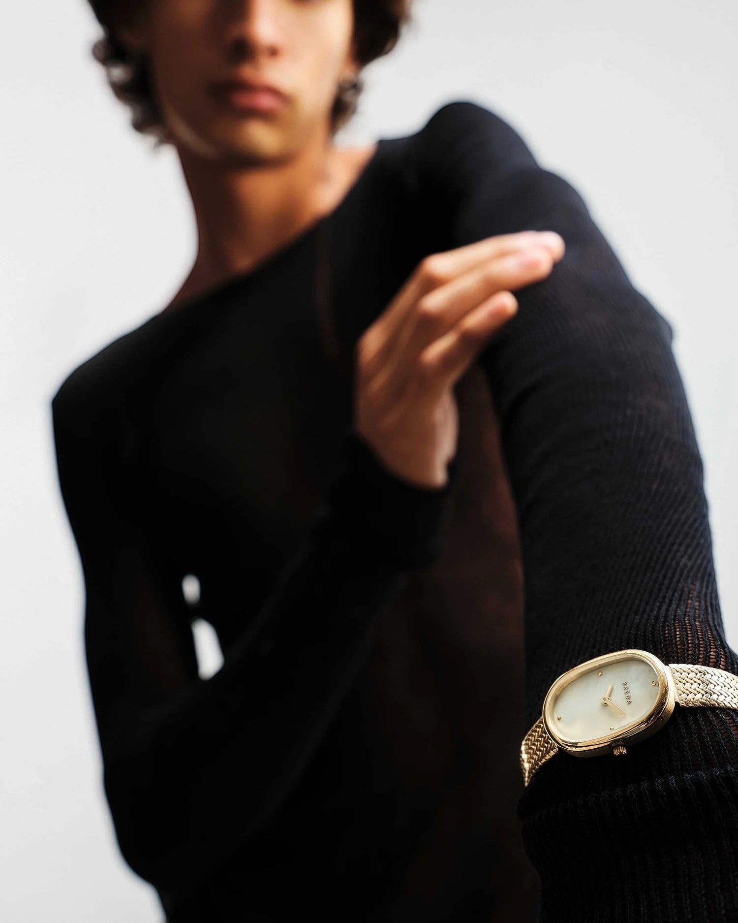 JONES + CO Jane Tethered watch with gold oval case, champagne mother-of-pearl dial, and woven mesh bracelet on wrist