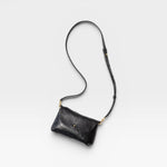 JONES + CO Kaanapali crossbody bag in black metallic aniline leather with adjustable strap and brass hardware.