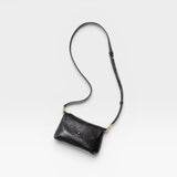 JONES + CO Kaanapali crossbody bag in black metallic aniline leather with adjustable strap and brass hardware.
