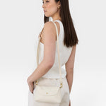 JONES + CO Kaanapali Crossbody in milk pebble leather, a small cream bag with gold hardware, worn by a woman.