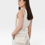 JONES + CO Kaanapali Crossbody in milk pebble leather, a small cream bag with gold hardware, worn by a woman.