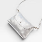 JONES + CO Kaanapali Crossbody in silver metallic aniline leather. Features a flap closure and adjustable strap.