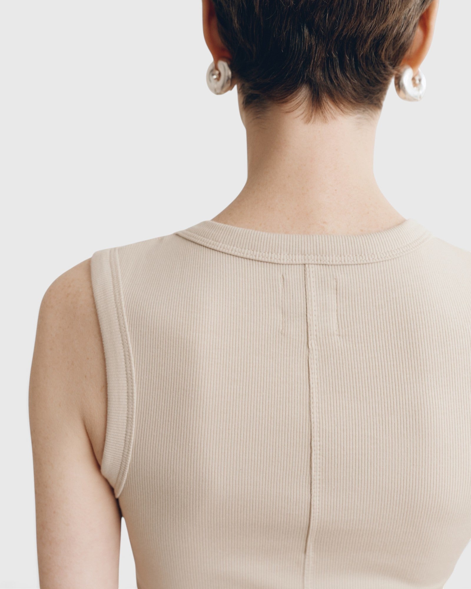 Back view of JONES + CO Kana Tank in dune beige, featuring a finely ribbed knit fabric and clean vertical seam detail.