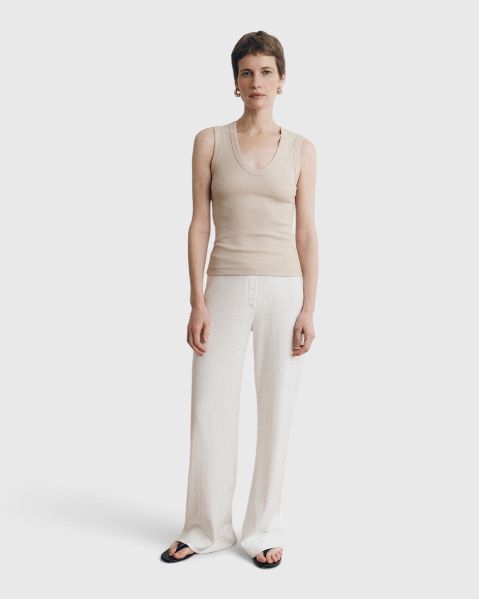 Model wearing a JONES + CO Kana Tank in dune beige, featuring a deep scoop neckline and ribbed knit fabric.