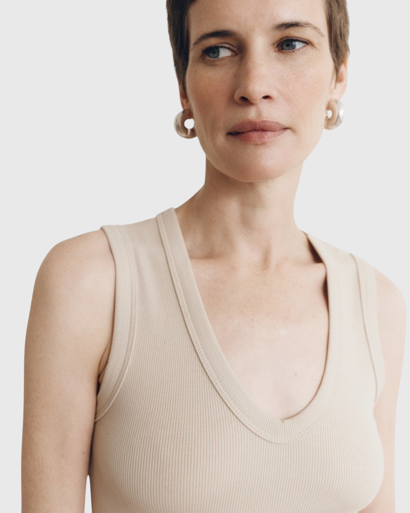 JONES + CO Kana Tank in dune beige featuring a deep scoop neckline and finely ribbed knit fabric on a model