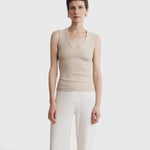 Model wearing a JONES + CO Kana Tank in dune beige with a deep scoop neckline and finely ribbed knit texture.