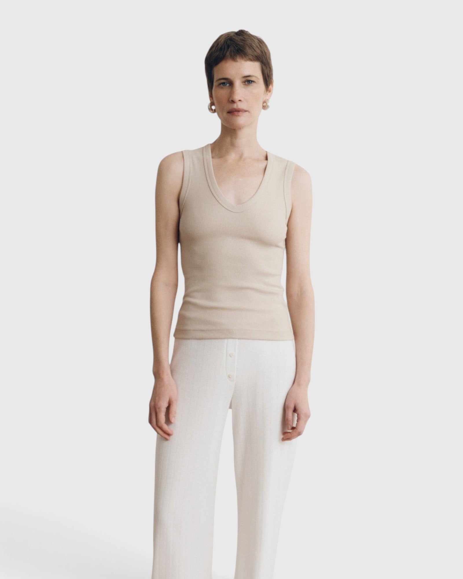 Model wearing a JONES + CO Kana Tank in dune beige with a deep scoop neckline and finely ribbed knit texture.