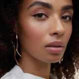 JONES + CO La Laque Tinted Lip Oil in a soft rose shade, worn by a model with curly hair.
