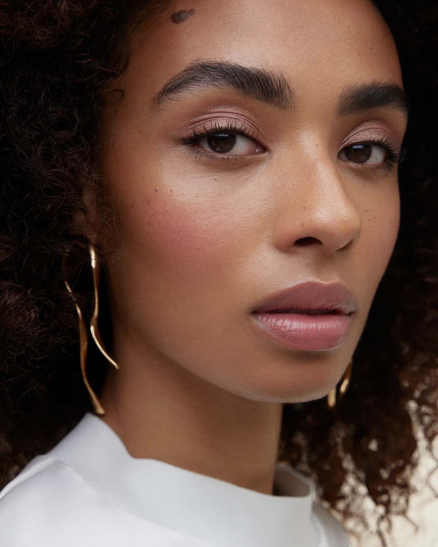 JONES + CO La Laque Tinted Lip Oil in a soft rose shade, worn by a model with curly hair.