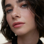 JONES + CO La Laque Tinted Lip Oil in a soft rose shade, worn by a model with blue eyes and freckles.