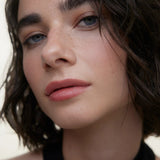 JONES + CO La Laque Tinted Lip Oil in a soft rose shade, worn by a model with blue eyes and freckles.