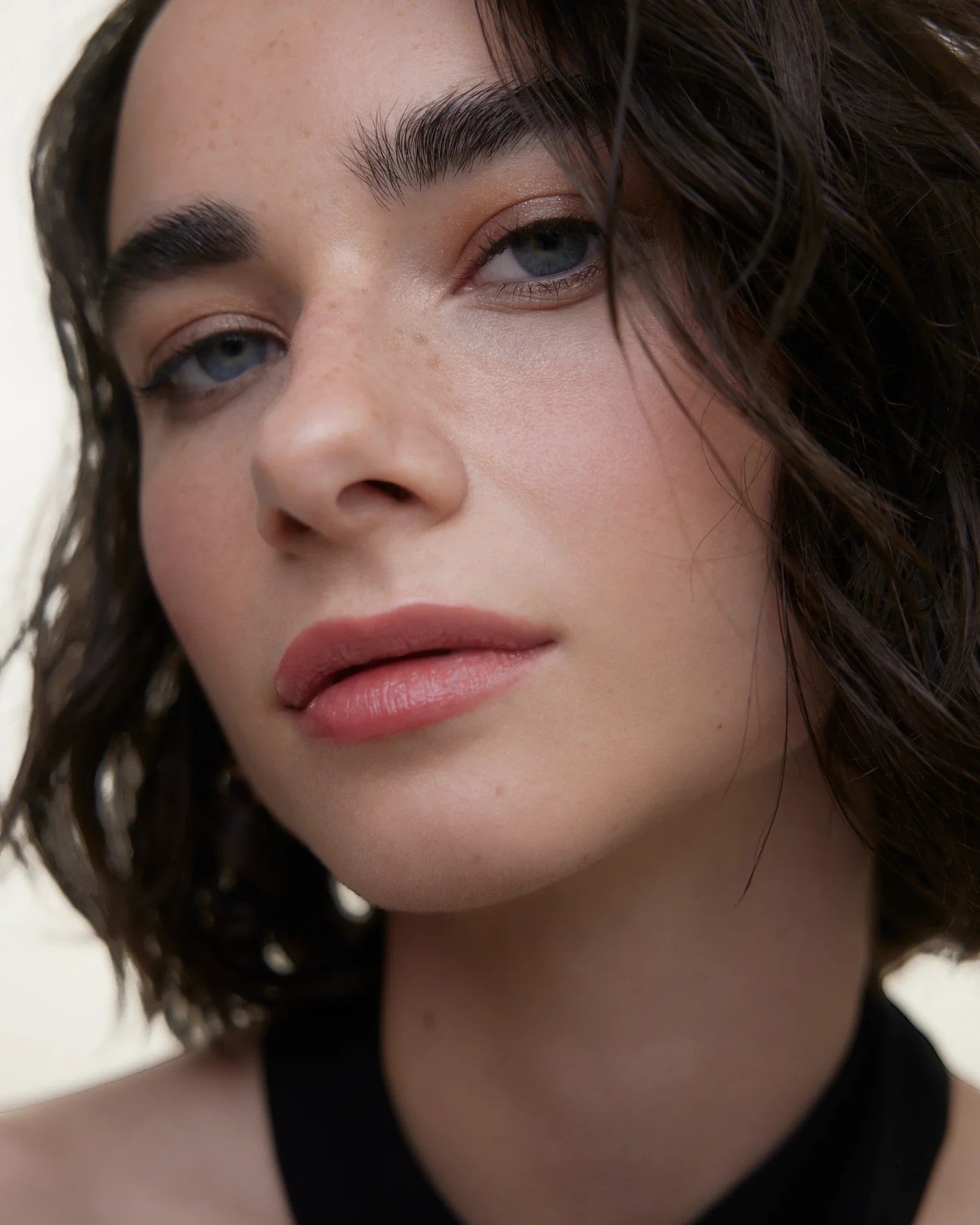 JONES + CO La Laque Tinted Lip Oil in a soft rose shade, worn by a model with blue eyes and freckles.