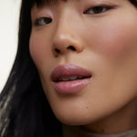 JONES + CO La Laque Tinted Lip Oil in a sheer rose shade, worn by a model with dark hair and subtle makeup.