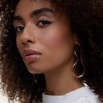 JONES + CO La Laque Tinted Lip Oil in a rosy nude shade, worn by a model with curly hair and gold earrings.