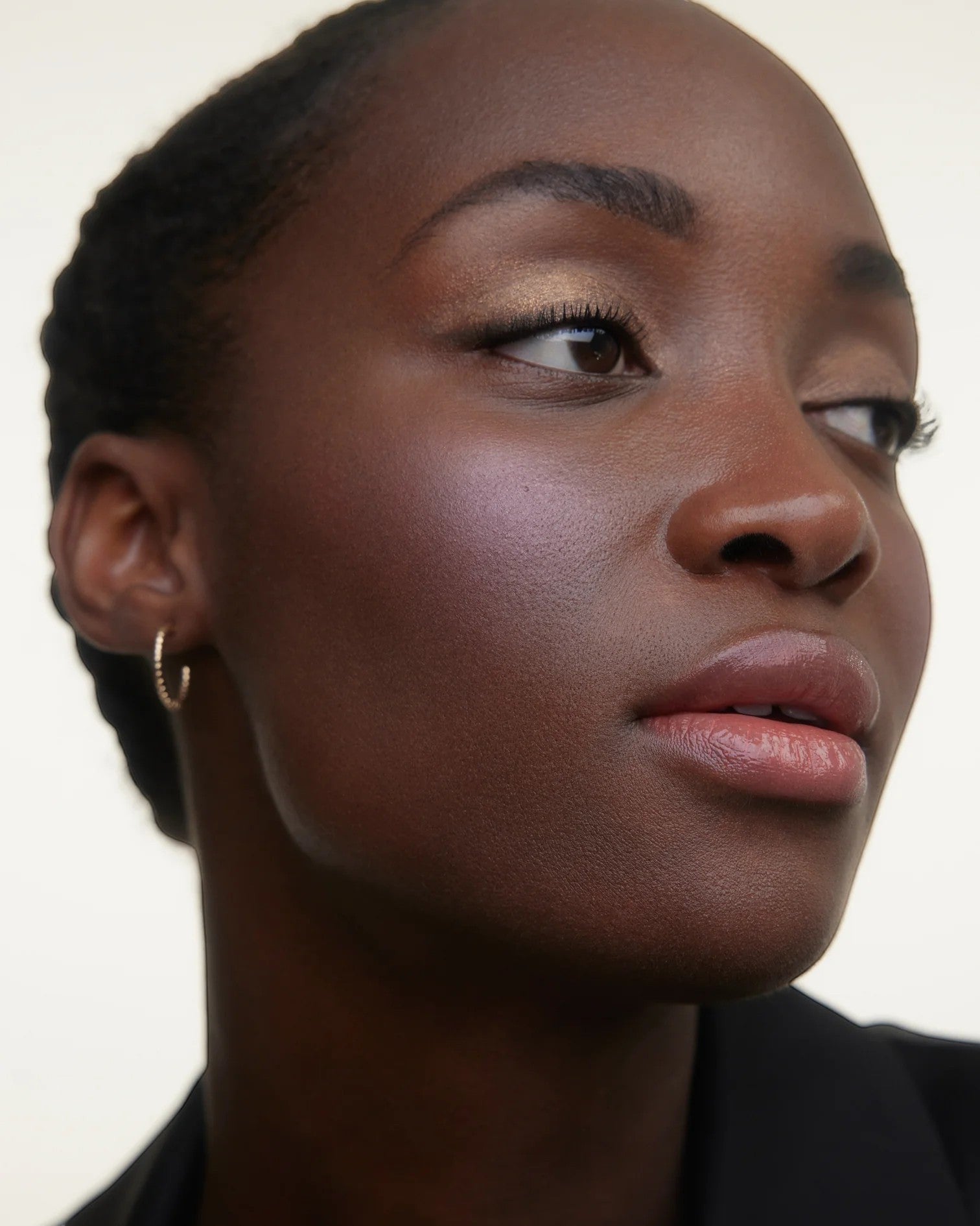 JONES + CO La Laque Tinted Lip Oil in a sheer, luminous rosy-nude shade, applied to a model with glowing skin and subtle shimmer.