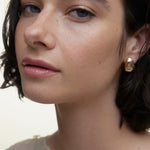 JONES + CO La Laque Tinted Lip Oil in a sheer rosy pink shade, worn by a model with natural makeup and gold earrings.
