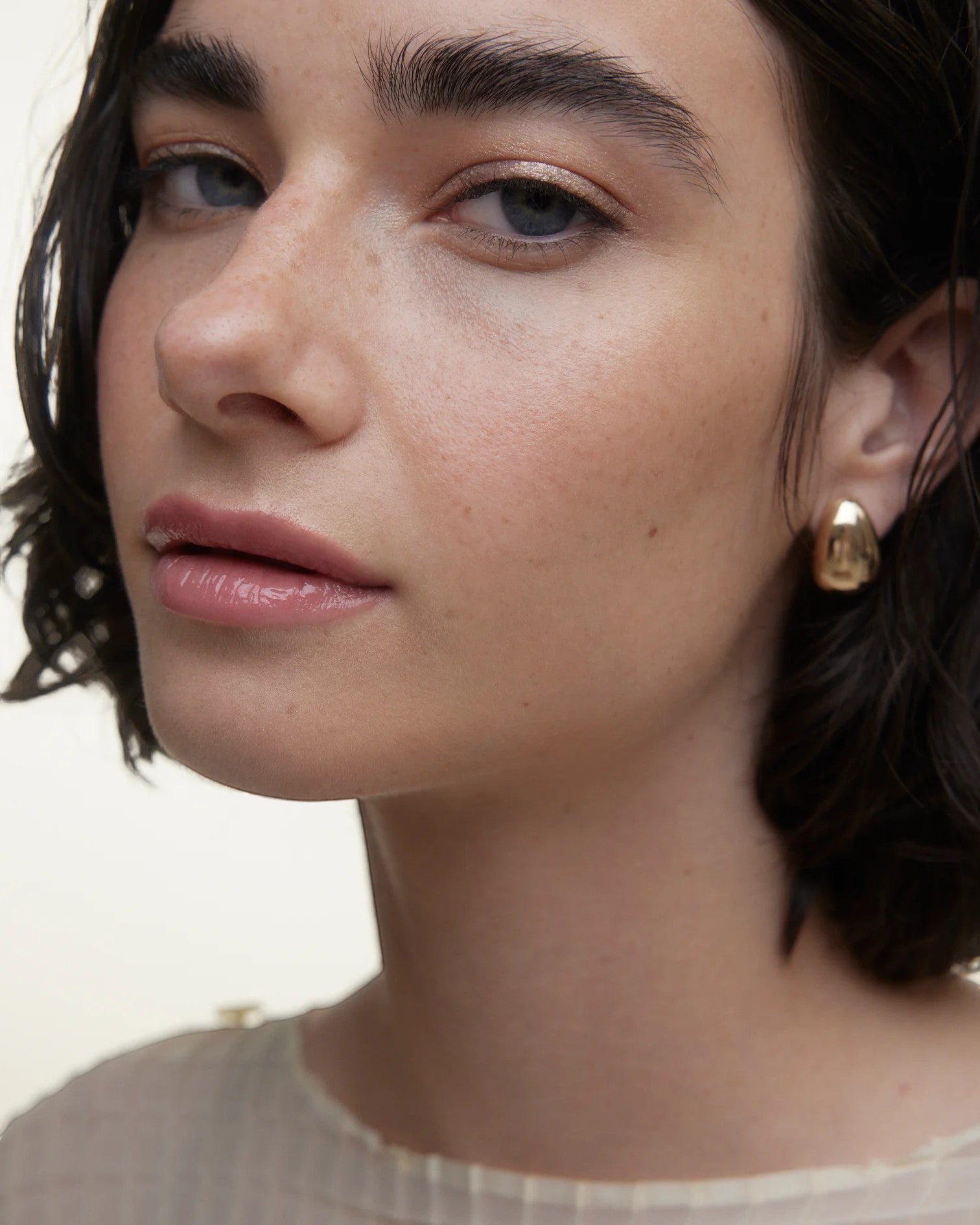 JONES + CO La Laque Tinted Lip Oil in a sheer rosy pink shade, worn by a model with natural makeup and gold earrings.