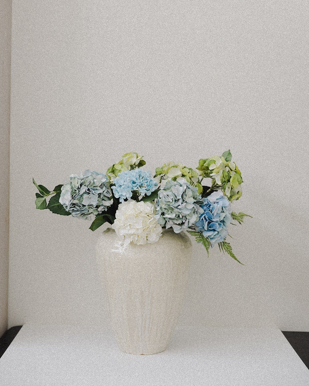 JONES + CO large ceramic vase with unique ash glaze, holding blue and green hydrangeas.