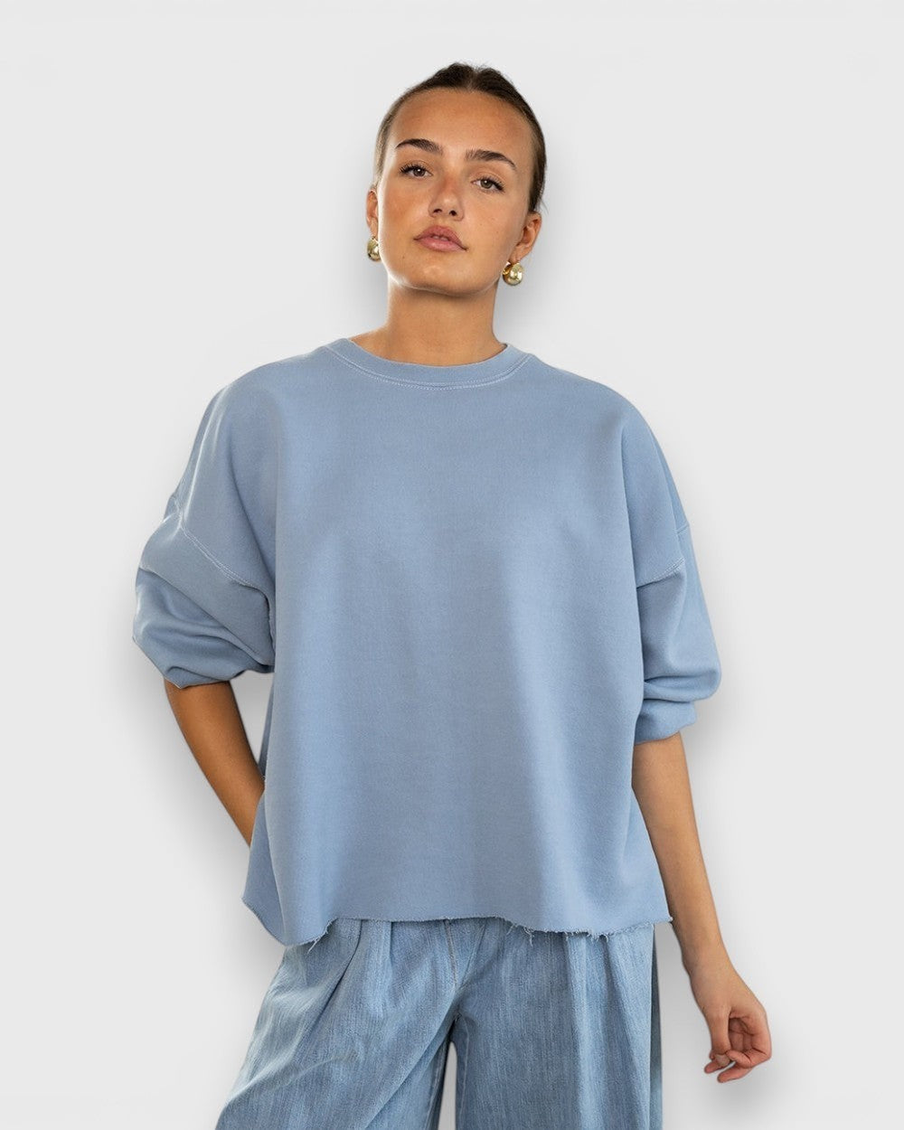 JONES + CO light blue crewneck sweatshirt with drop shoulders, cropped sleeves, and a raw edge hemline on a model.