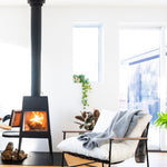 JONES + CO light grey alpaca wool blend throw blanket draped over a white armchair next to a fireplace.