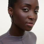 JONES + CO La Laque Tinted Lip Oil in a sheer, luminous nude shade on model with hoop earrings.