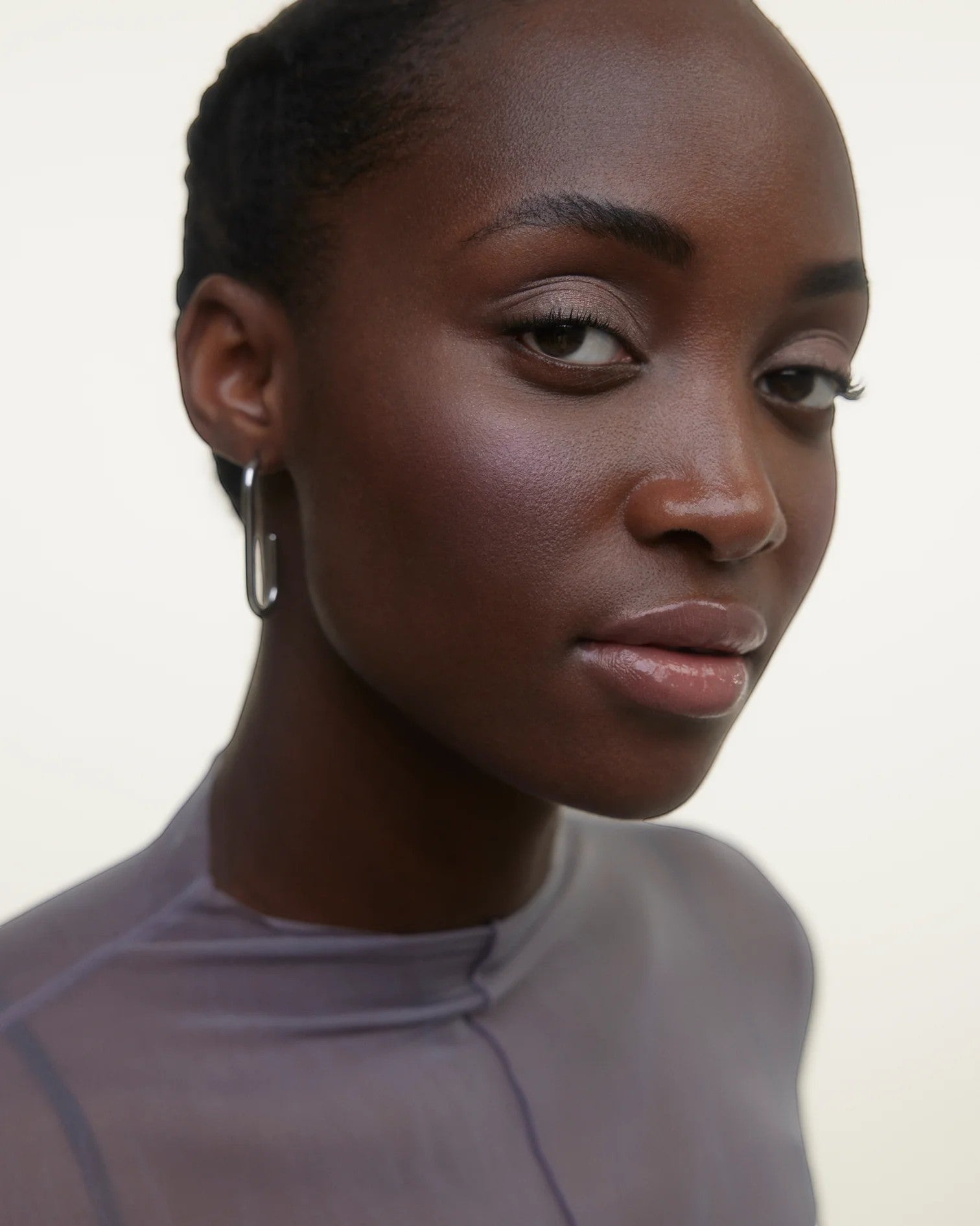 JONES + CO La Laque Tinted Lip Oil in a sheer, luminous nude shade on model with hoop earrings.