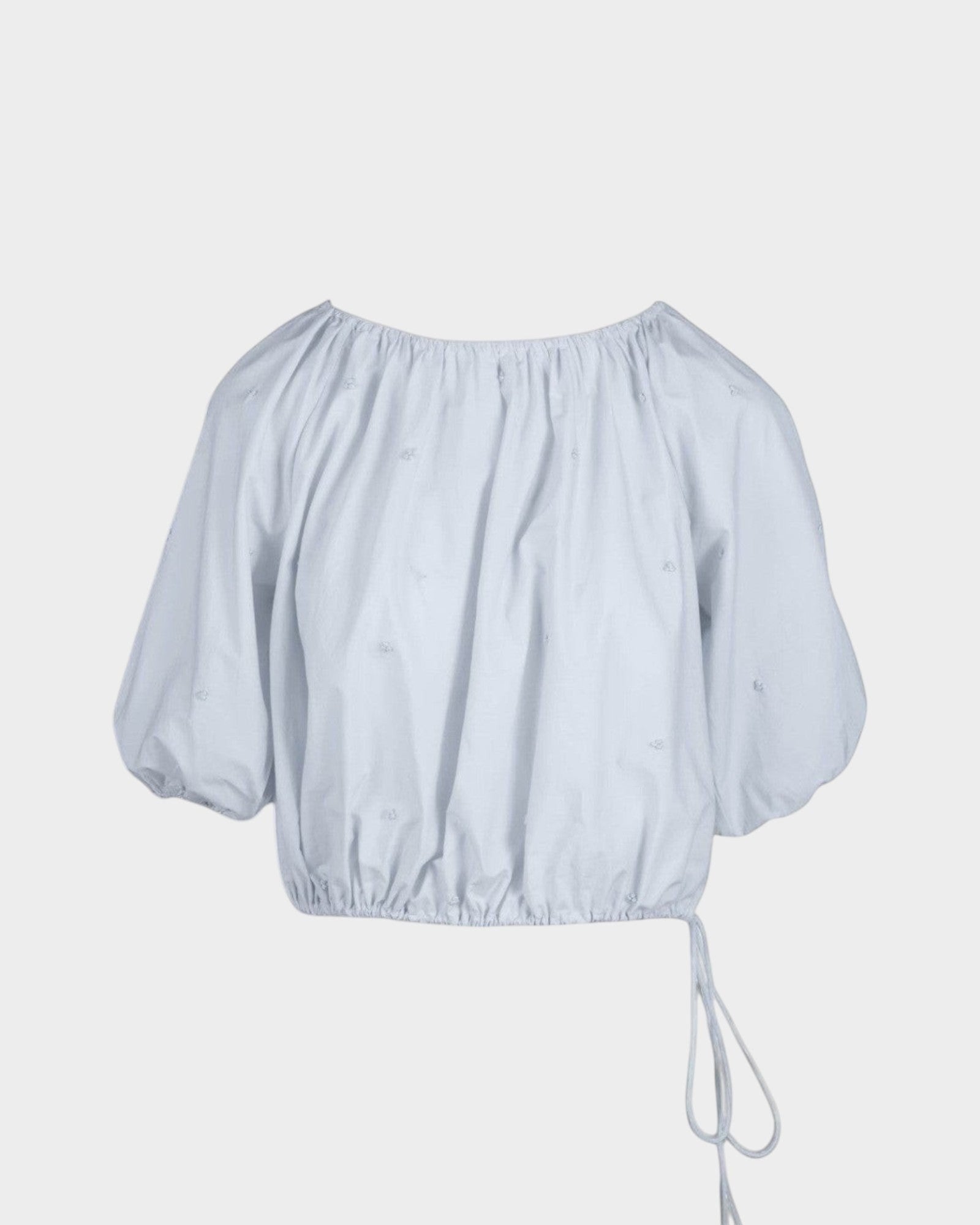 JONES + CO Lotus cropped blouse in light blue with short puff sleeves, drawstring waist, and French knot embroidery.