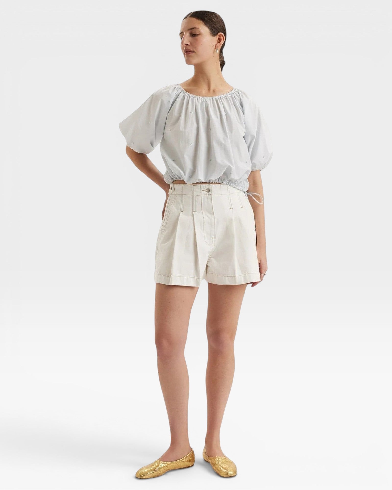 JONES + CO light blue cropped Lotus top with short sleeves, gathered cuffs, and drawstring waist. Features French knot embroidery.